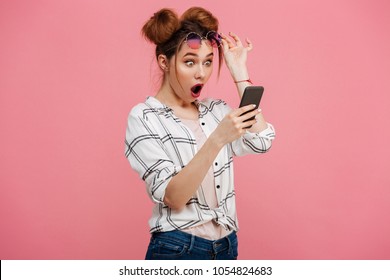 Portrait of a shocked young girl using mobile phone isolated over pink background - Shutterstock ID 1054824683