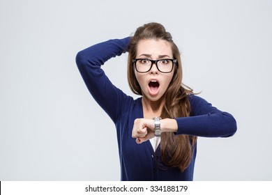 Portrait of shocked young woman holding hand with wrist watch and looking at camera isolated on a white background