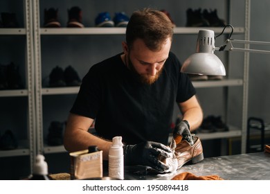 Portrait Of Shoemaker Cleaning With Brush And Foam On Old Light Brown Leather Shoes. Man Wipes Off Excess Foam With Rag. Concept Of Cobbler Artisan Repairing And Restoration Work In Shoe Repair Shop.