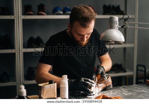 Portrait of shoemaker cleaning with brush and foam\
on old light brown leather shoes. Man wipes off excess foam with\
rag. Concept of cobbler artisan repairing and restoration work in\
shoe repair shop.