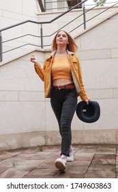 Portrait shooting of a stylish girl. Beige shades. Trends of spring and summer 2020.Black pants and mustard (orange) top. Brown denim jacket with faux fur.Black hat. 