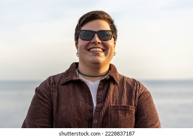 Portrait of a short haired non binary curvy woman with a genuine toothy smile wearing sunglasses - gender fluid people lifestyle concept - Powered by Shutterstock