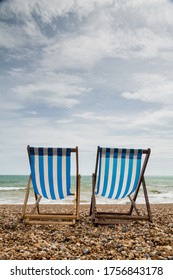 Portrait shot of 2 stripy blue and white deck chairs on an empty shingle beach looking out to sea. Taken in Brighton, England, UK