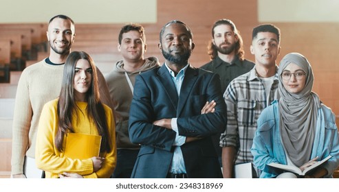 Portrait shot of African American male happy professor among mixed-races students in auditorium of University laughing n front of camera. Teacher and pupils concept. Posing for photo. - Powered by Shutterstock