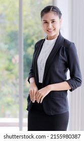 Portrait shot of Asian successful confident happy female entrepreneur with braids hairstyle in formal black jacket suit stand smiling posing on chest look at camera in front glass window.