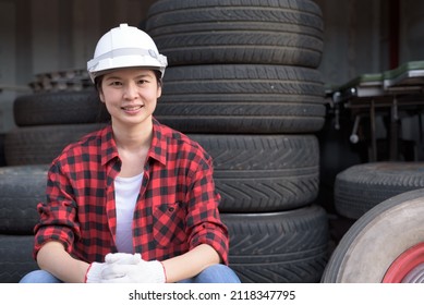 Portrait Shot Of An Asian Woman Wearing Red Lumberjack Shirt And Safety Hardhat Sitting, Smiling, Relaxing, Looking At Camera. Female Worker Or Engineer Portrait At The Tire Shop.