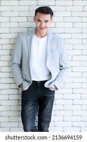 Portrait Shot Asian Young Cool Smart Handsome Muscular Undercut Hairstyle Male Businessman In Casual Gray Suit Jacket Standing Holding Hands In Jeans Pockets Look At Camera On Brick Wall Background.