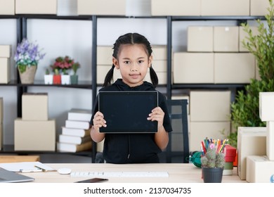 Portrait shot of Asian young primary schoolgirl in casual outfit standing smiling holding showing black blank screen monitor touchscreen tablet computer in hands for advertising copy space and text.