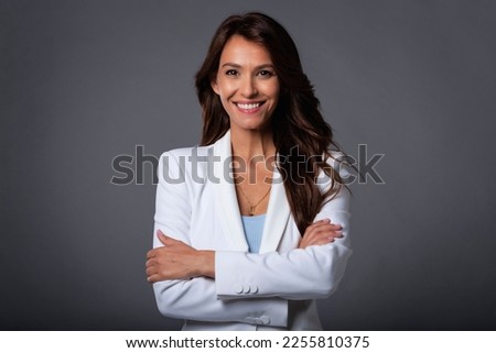 Portrait shot of an attractive brunette woman wearing white blazer while standing at isolated grey background. Copy space.