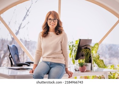 Portrait shot of attractive mature businesswoman looking at camera and smiling while standing at desk at the office. - Shutterstock ID 2184966743