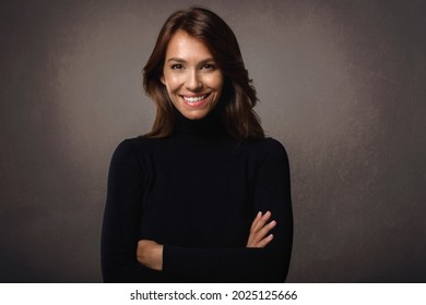 Portrait shot of attractive middle aged woman wearing turtleneck sweater and laughing while standing at isolated dark grey background. Copy space.