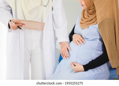 Portrait Shot Of An Attractive Smiling Adult Muslim Doctor Wearing Cream Hijab With Stethoscope Around Neck Standing And Talking To Islam Pregnant Woman.