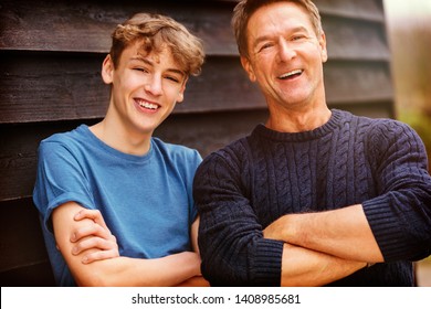 Portrait Shot Of An Attractive, Successful And Happy Middle Aged Man Father Male Arms Folded With His Teenage Boy Son Outside Laughing Teen, Wearing A Blue Sweater And T Shirt