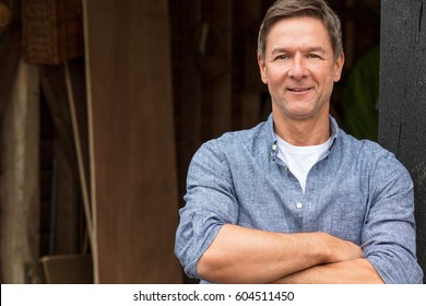 Portrait Shot Of An Attractive, Successful And Happy Middle Aged Man Male Arms Folded Outside Wearing A Blue Shirt Outside His Garage Or Shed
