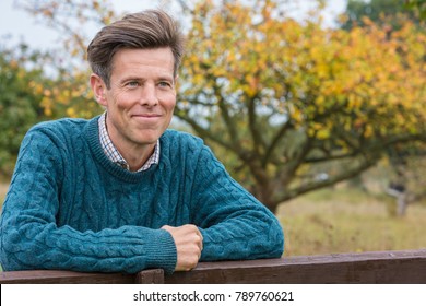 Portrait Shot Of An Attractive, Successful And Happy Middle Aged Man Male Arms Folded Outside Leaning On A Fence Or Gate In The Country