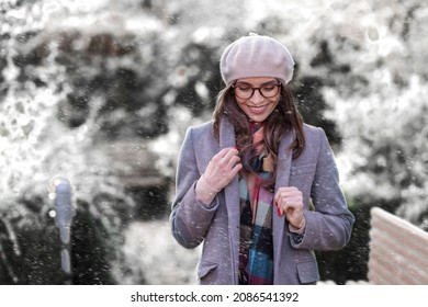 Portrait shot of attractive young woman wearing beret hat and winter coat while standing outside and enjoy falling snow.