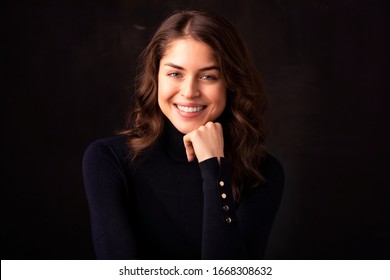 Portrait Shot Of Beautiful Young Woman Wearing Turtleneck Sweater While Looking At Camera And Smiling At Isolated Dark Background. 