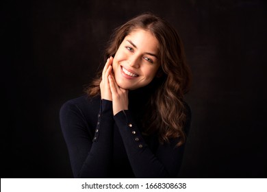 Portrait Shot Of Beautiful Young Woman Wearing Turtleneck Sweater While Looking At Camera And Smiling At Isolated Dark Background. 