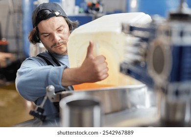 Portrait shot of concentrated male production worker pouring liquid from plastic container into stainless steel tank making craft cider in workshop of factory, copy space - Powered by Shutterstock