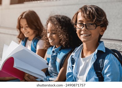 Portrait shot of cute little children preteen boys and girls pupils kids with backpacks and notebooks sitting on the stairs outdoors. Boy smiling looking at camera. Elementary middle school education - Powered by Shutterstock