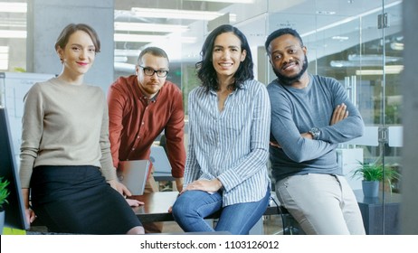 Portrait Shot Of A Diverse Group Of Talented Young Professionals Sitting On A Desk In The Stylish Modern Environment. Real People Sincerely Smiling On Camera.