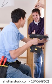 A Portrait Shot Of An Electrician Talking With His Co-worker While Drilling An Outlet In The Wall.