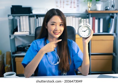 Portrait Shot Of Female Doctor With Office Clock In Doctor’s Office. Time Concept.