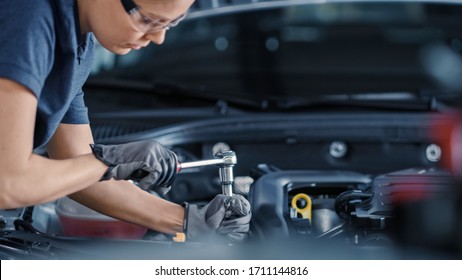 Portrait Shot of a Female Mechanic Working on a Vehicle in a Car Service. Empowering Woman Fixing the Engine. She is Wearing Gloves and Using a Ratchet. Modern Clean Workshop.