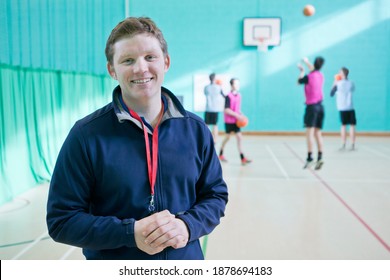 Portrait shot of a gym teacher standing in a gym with high school students playing basketball in the background. - Powered by Shutterstock