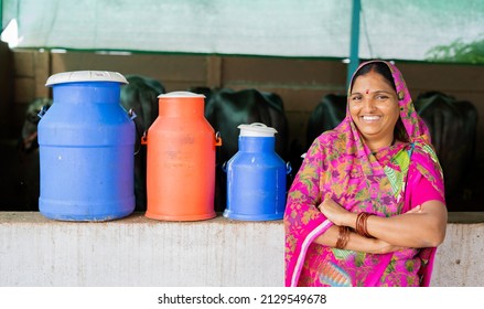 Portrait shot of happy Indian milk dairy woman farmer with milk containers and cattles behind looking at camera - concept of empowerment, village lifestyle and leadership