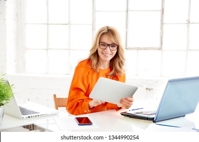 Portrait shot of happy mature businesswoman holding digital tablet i her hand and working while sitting at office desk.