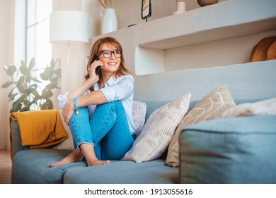 Portrait shot of happy mature woman talking with somebody on her mobile phone while relaxing at home on the couch. 