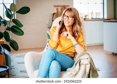 Portrait shot of happy mature woman talking with somebody on her mobile phone while relaxing at home in the armchair. 