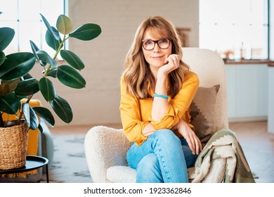 Porträtaufnahme einer glücklichen Frau mittleren Alters, die sich zu Hause im Sessel entspannt.
