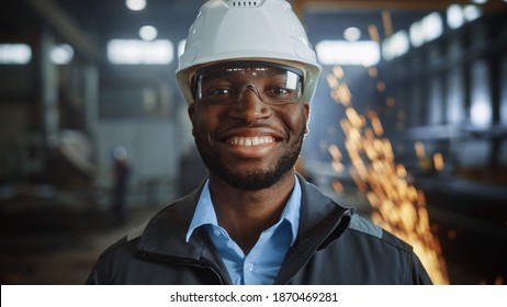 Portrait Shot of Happy Professional Heavy Industry Engineer Worker Wearing Uniform, Glasses and Hard Hat in Steel Factory and Smiling on Camera. Industrial Specialist in Metal Construction Manufacture