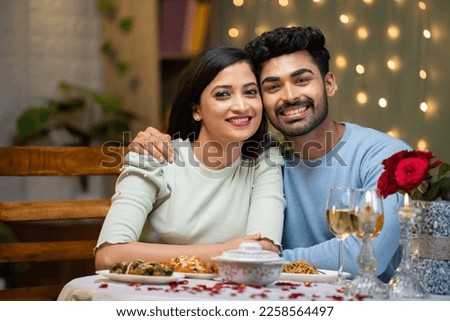 Portrait shot of happy smiling couple looking at camera during candle light dinner at home - concept of celebrating valentines day, affection and dating