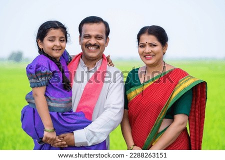 Portrait shot of Happy smiling Indian village farming couple with kid standing by looking at camera near paddy farmland - concept of relationship,family harmony and togetherness