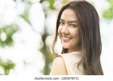 Portrait Shot Of Happy, Successful, Attractive Asian Woman Having Big Smiling And Nice Teeth With Confident Look Toward The Camera At A Blurry Park Background With Copy Space In Natural Sunlight.