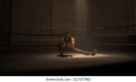 Portrait Shot Of An Isolated Female Kickboxer Stretching In The Middle Of A Boxing Ring Before Starting Her Training And Sparring Sessions With Her Coach, Preparing For The Competition. Martial Arts.