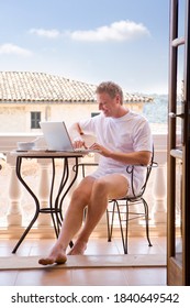 A Portrait Shot Of A Man In Boxer Shorts Using A Laptop In His Balcony.