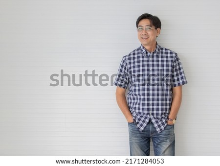 Portrait shot of middle aged asian male model with short black hair wearing blue plaid shirt with stand smiling in front of white stripe background put his hands in jeans pocket.