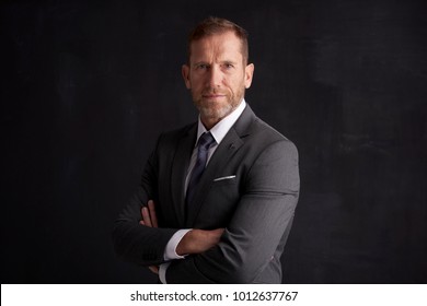Portrait shot of a middle aged businessman wearing suit while standing with arms crossed at dark background.