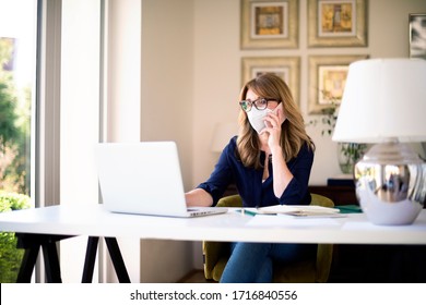 Portrait shot of middle aged woman wearing face mask while working at home on her notebook and making a call during coronavirus pandemic.  - Shutterstock ID 1716840556