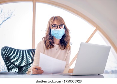 Portrait shot of middle aged woman wearing face mask while working at the office on her computer during coronavirus pandemic.  - Powered by Shutterstock