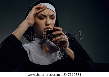 Portrait shot of a nun, sitting on a chair. She's wearing dark nun's clothing. The nun is drinking wine, her eyes are closed. Her right hand is at her forehead. 