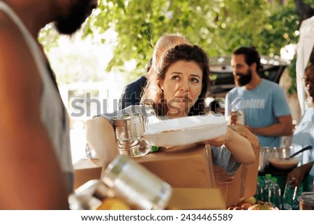 Portrait shot of poor and needy caucasian woman carrying her donation box and canned goods from food bank. Image showing the underprivileged and homeless people receiving support from charity group.