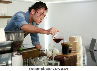 Portrait Shot Professional Asian Man Barista With Glasses Concentrate Mix Coffee And Tea By Filled Cup With Ice At Bar Counter. The Ways To Brewing Coffee. Coffee Shop Barista Brewing Concept.