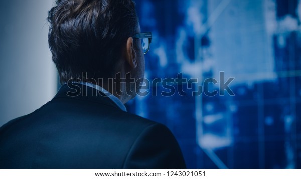 Portrait Shot of the Special Agent\
in Charge Looking at Satellite Surveillance Footage of the Car\
Chase. GPS Tracking Fugitive in the Big Monitoring\
Room.