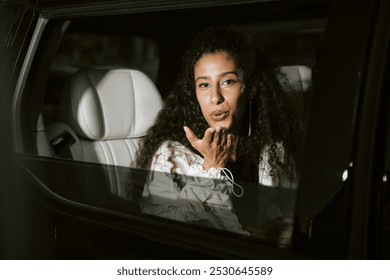 Portrait shot through open limousine window of Middle Eastern female celebrity looking at paparazzi playfully answering public attention with blowing kiss while leaving ceremony, camera flash - Powered by Shutterstock