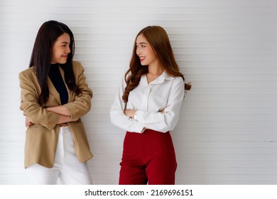 Portrait Shot Of Two Young Asian Office Workers In Formal Clothes Standing, Crossed Arm And Looking At Each Other And Talking With A Cute Smiling On White Background. Close Friends And Team Concept.